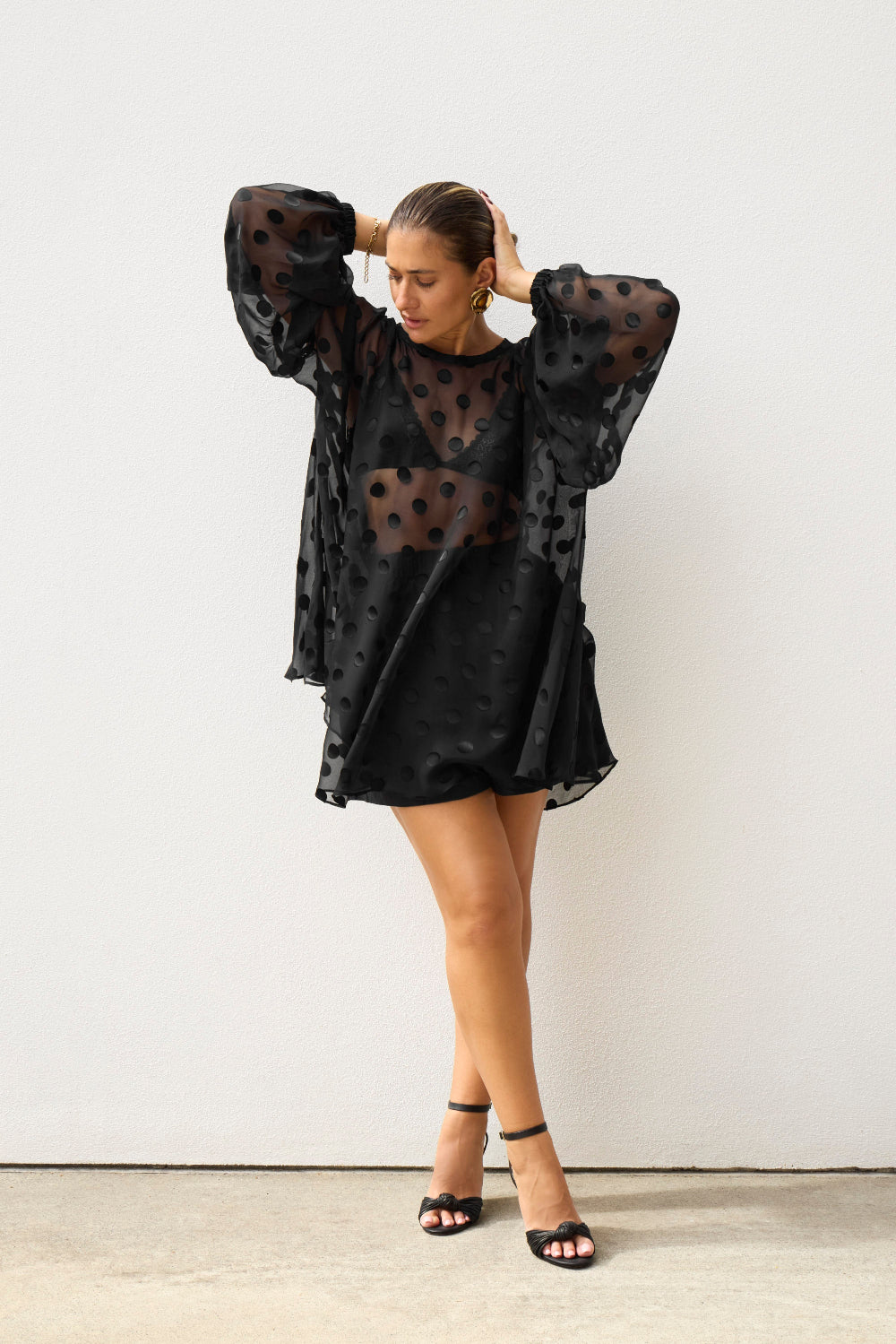 Woman wearing a black sheer dress with long sleeves against a white background