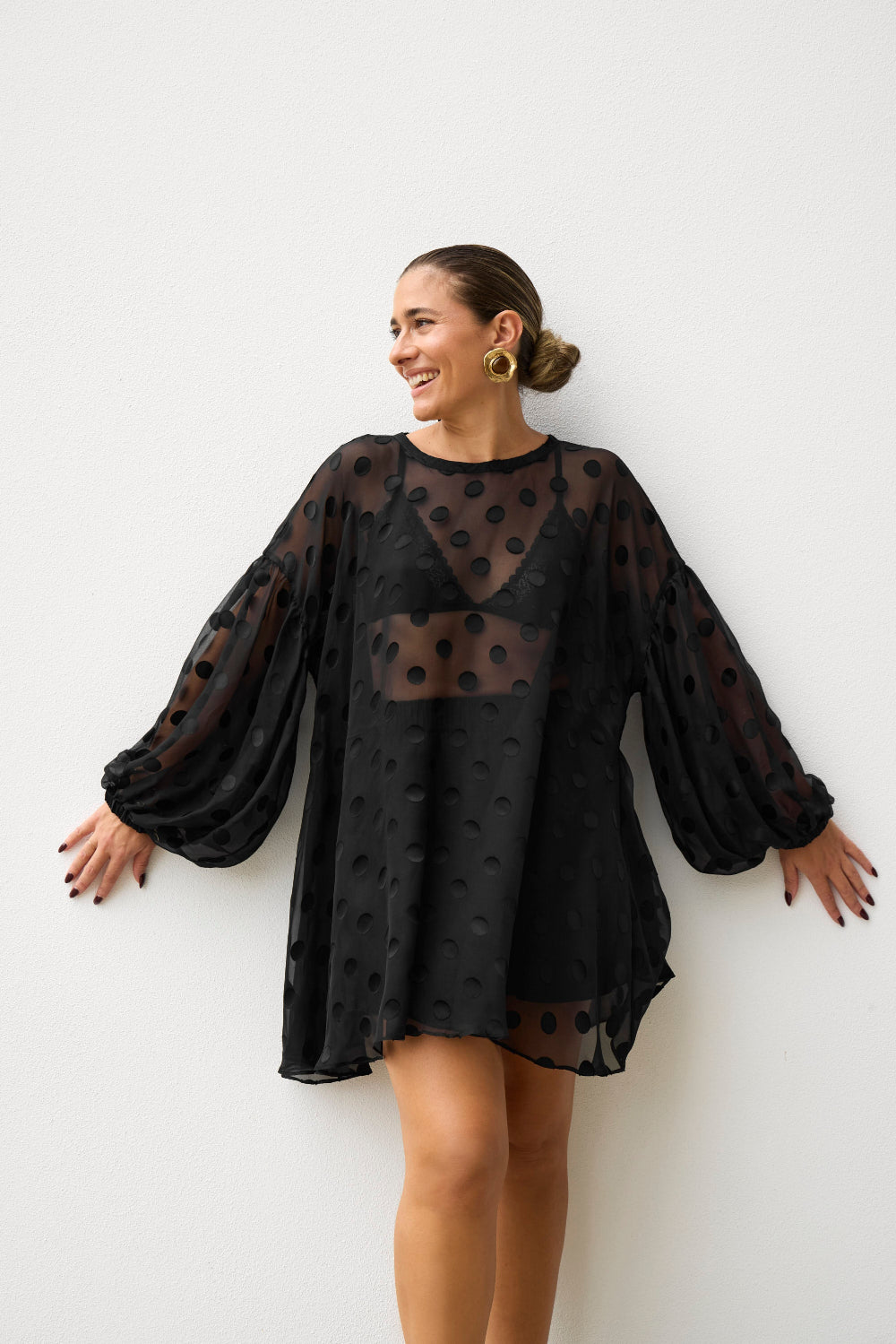 Woman wearing a black sheer dress with long sleeves against a white background