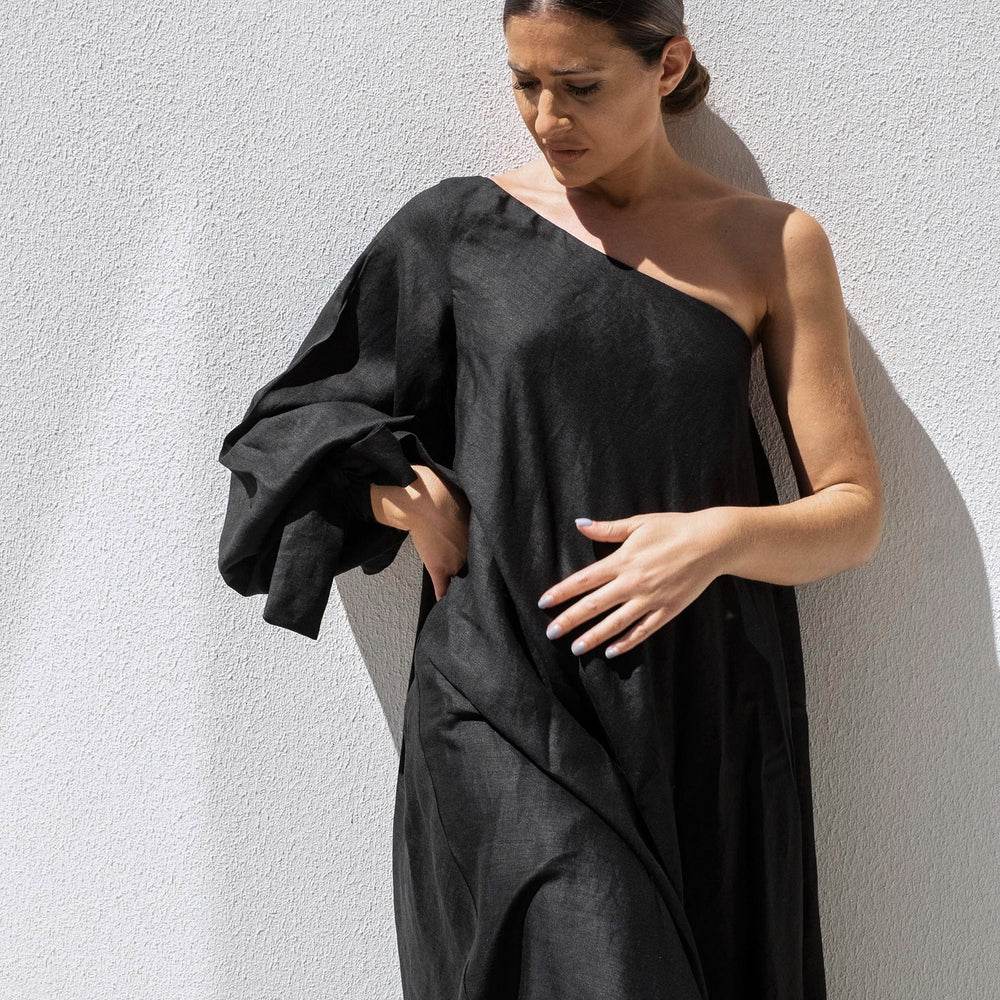 
                      
                        A woman with dark hair tied back wears an Isabella Longginou Black Balloon Sleeve Swing Dress. Posing against a white wall, she looks down, adjusting the fabric of the dress as sunlight casts a shadow behind her.
                      
                    